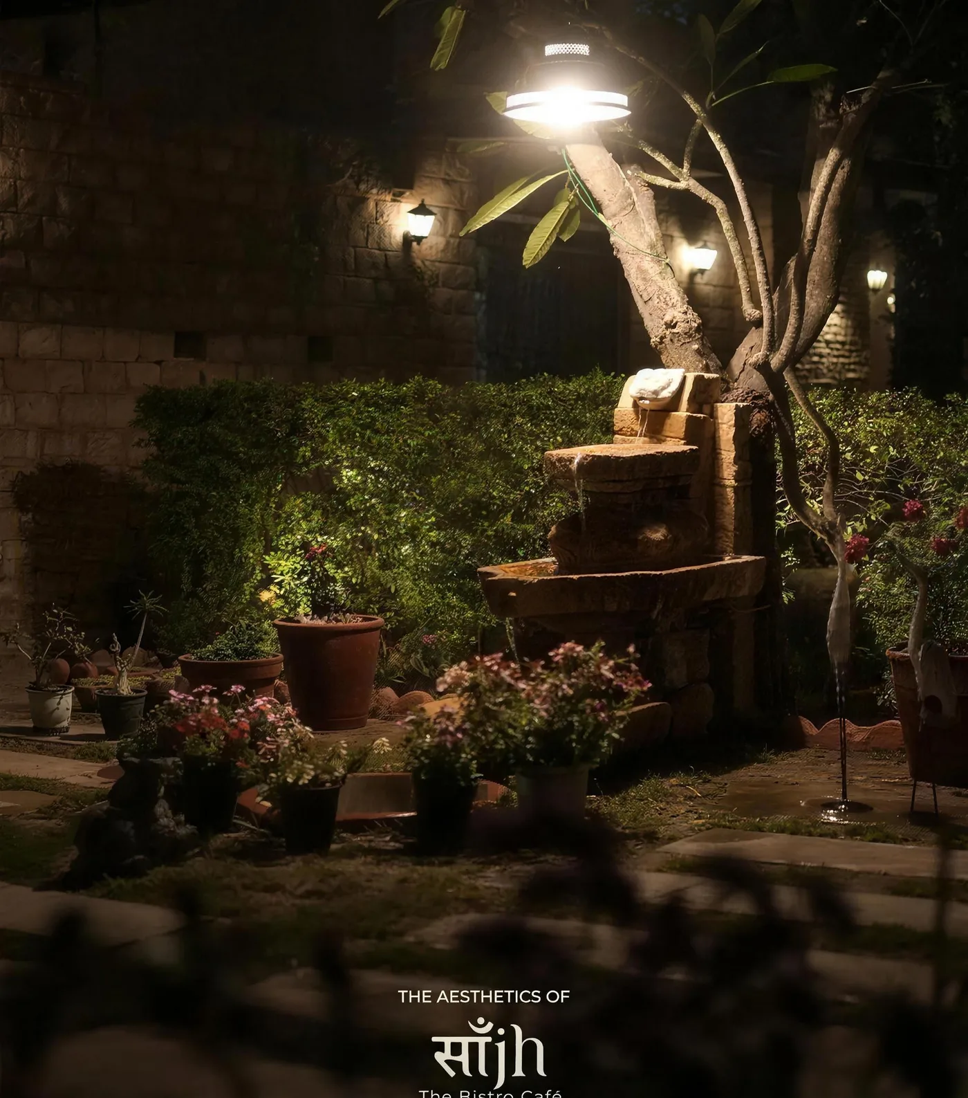 The garden courtyard at night, a tree strung with lights above potted plants and stone paving at Saanjh The Bistro, Jodhpur