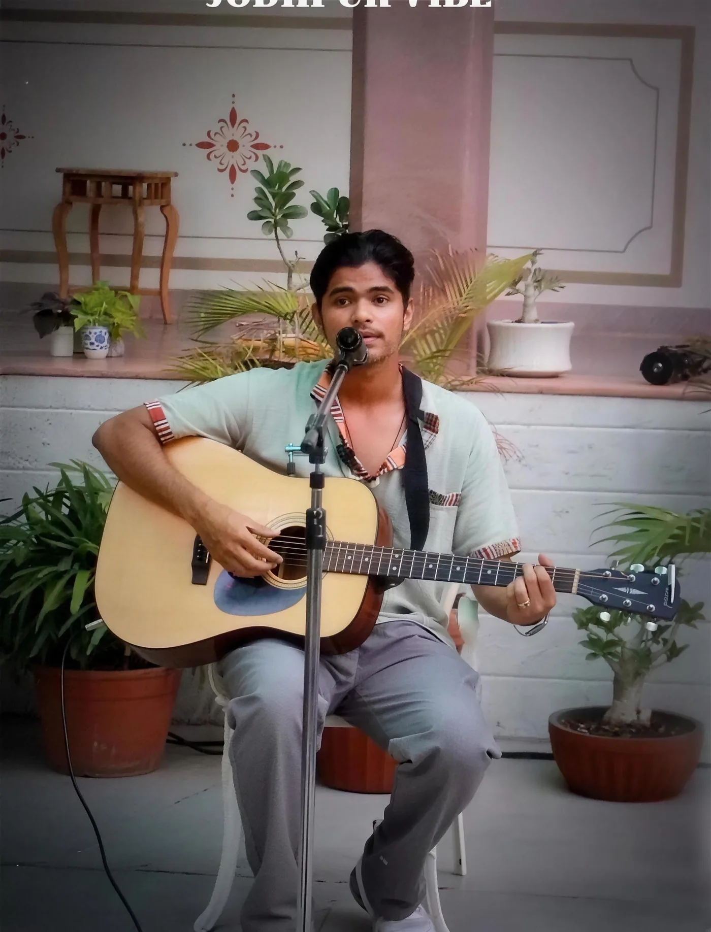 A guitarist playing on the arched terrace beside potted plants and a sunburst mirror at Saanjh The Bistro, Jodhpur