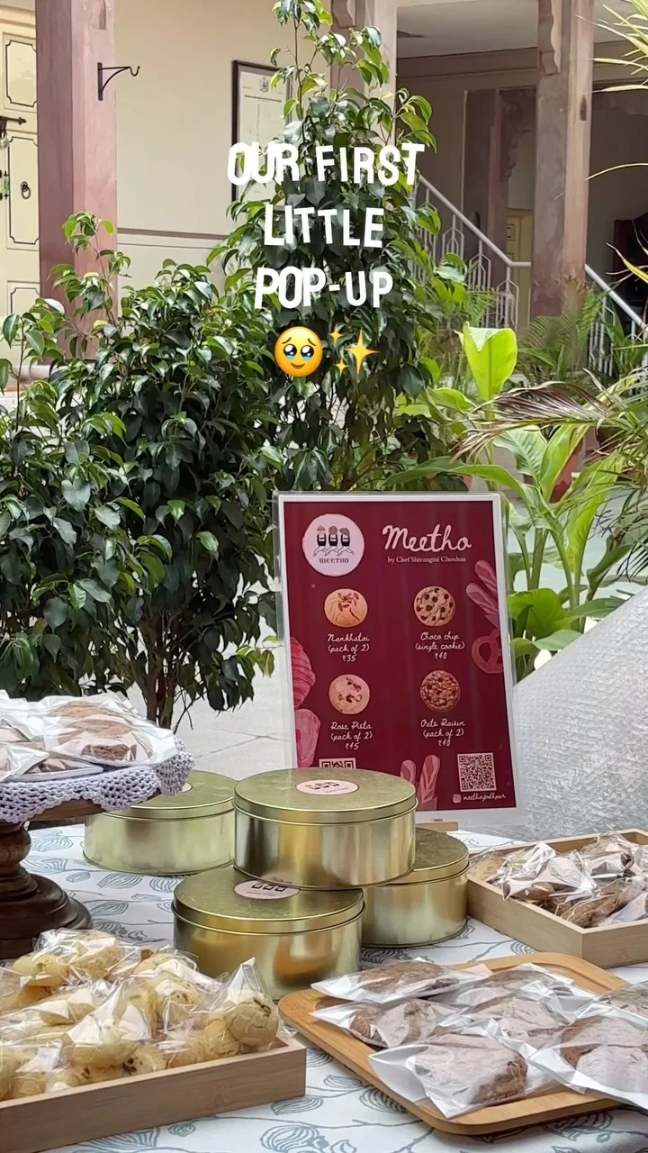 A bake sale table of tins and packaged cookies set up in the sandstone courtyard at Saanjh The Bistro, Jodhpur