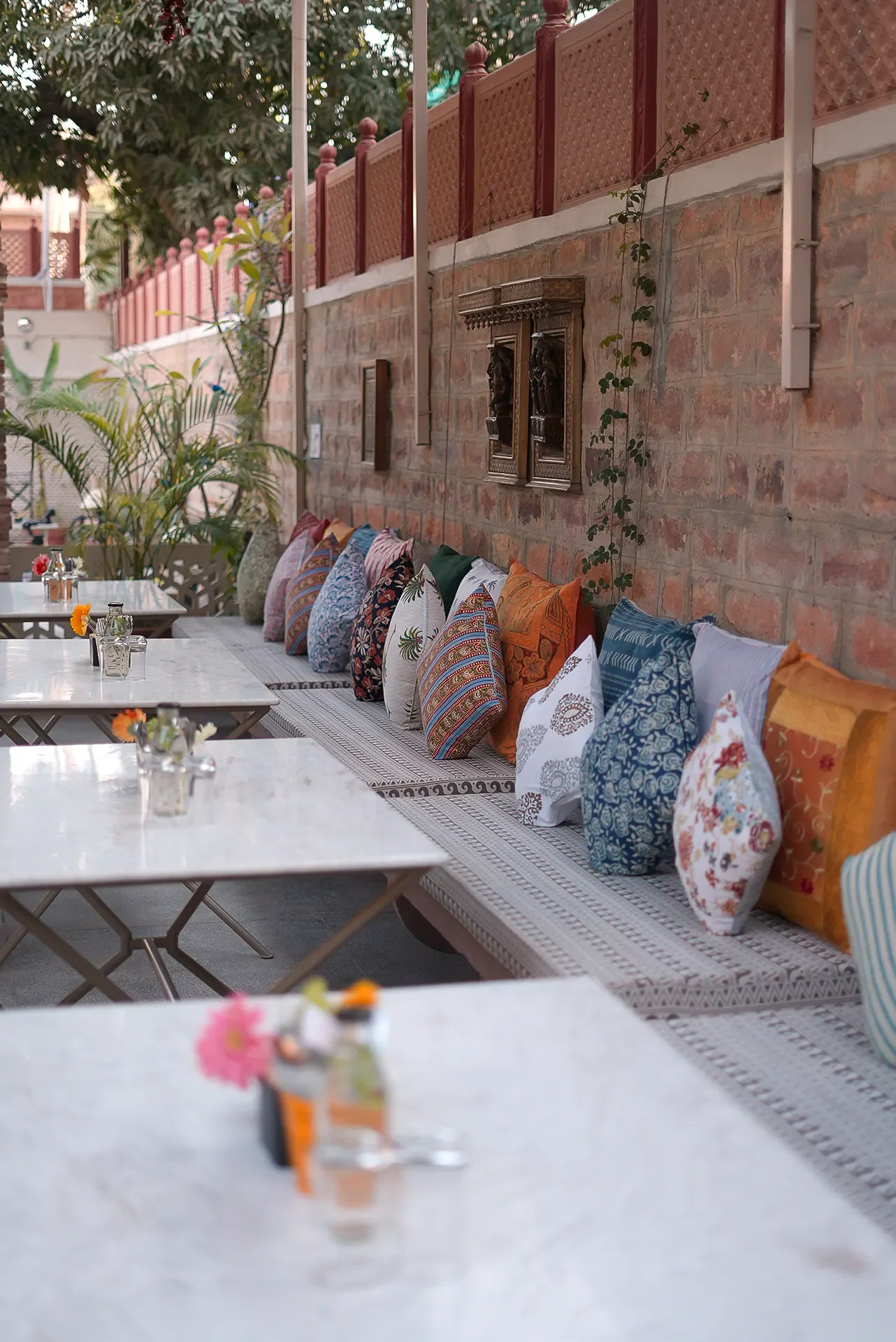 A long communal table lined with colourful block-print cushions against the sandstone wall of the courtyard at Saanjh The Bistro, Jodhpur