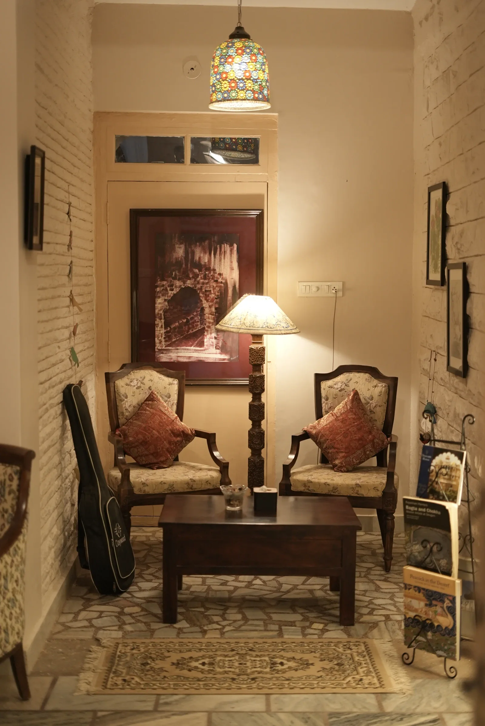 Two upholstered armchairs beside a table lamp and framed prints in the indoor lounge at Saanjh The Bistro, Jodhpur