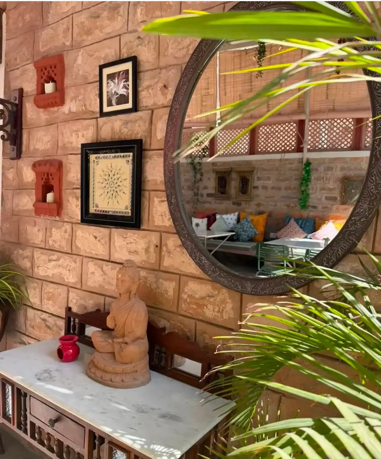 A round mirror and framed artwork hung on the sandstone brick wall above a console at Saanjh The Bistro, Jodhpur